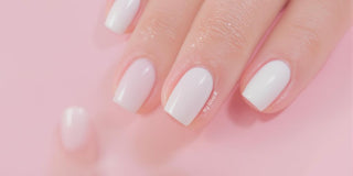 White nail polish on elegant nails against a pastel background.