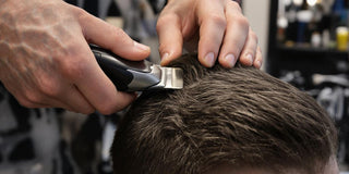 Person using clippers on client's hair in barbershop.